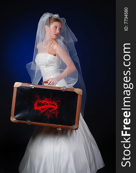 Young bride with heavy travelling bag on a black background