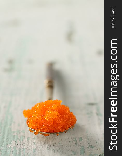 Red japanese caviar on a spoon, closeup for texture with wooden background.