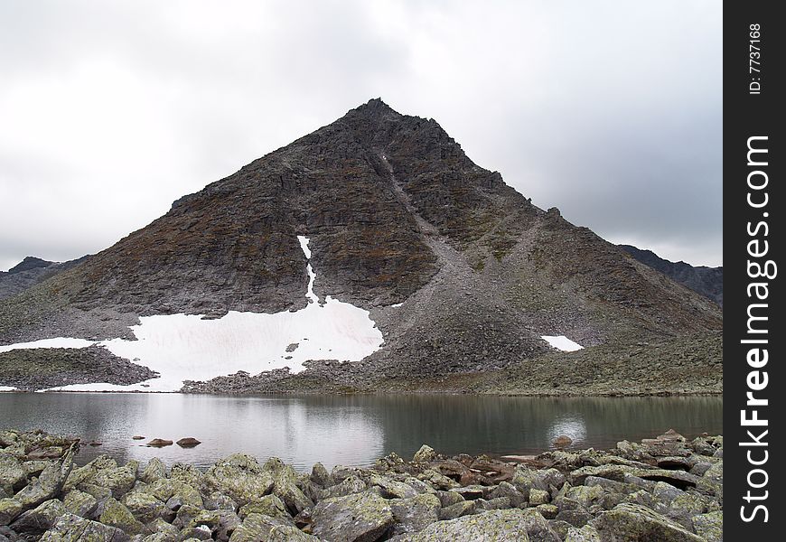 Photo. The mountain, reflecting in the lake. Cloudy skies. Stones.