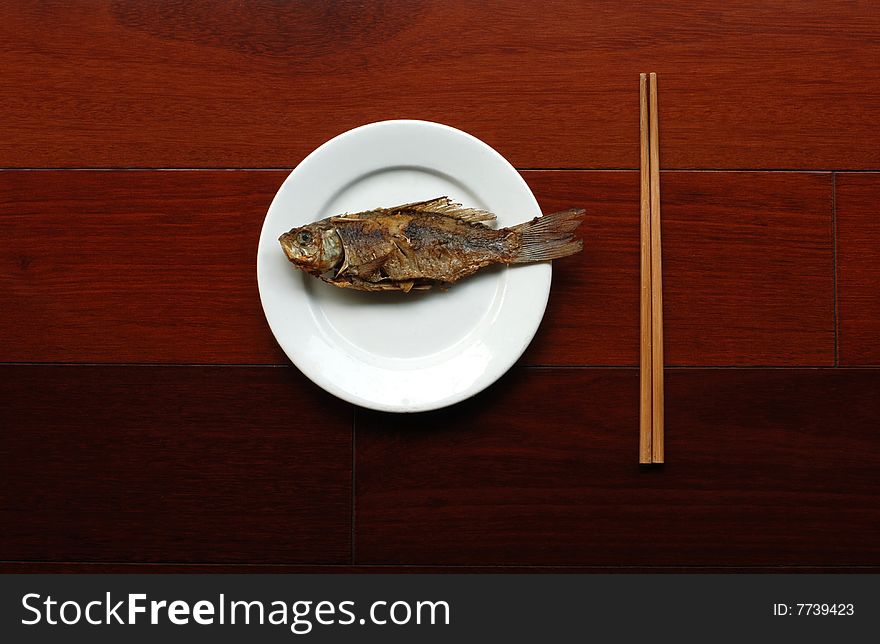 Fried crucian  in white plate with chopsticks on wooden tabie