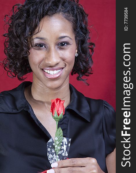 A young adult black woman on a red background, smiling while holding a rose. A young adult black woman on a red background, smiling while holding a rose