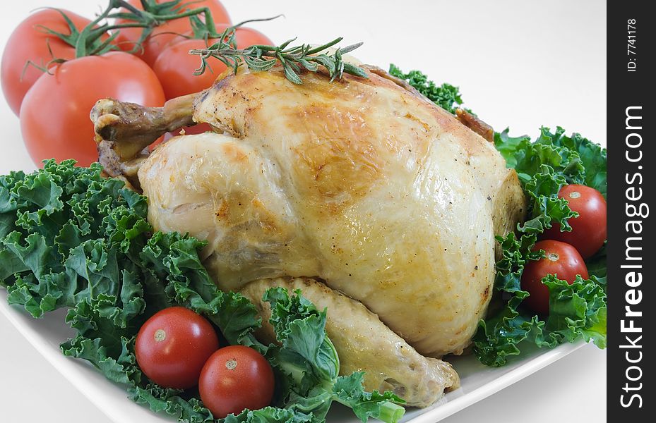 Whole roasted chicken garnished with kale, cherry tomatoes, and rosemary