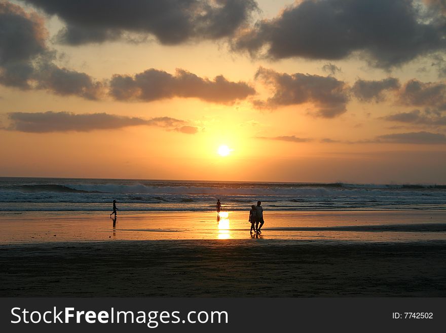 Sun setting over a sandy beach in Bali. Silhouettes of people walking. Sun setting over a sandy beach in Bali. Silhouettes of people walking