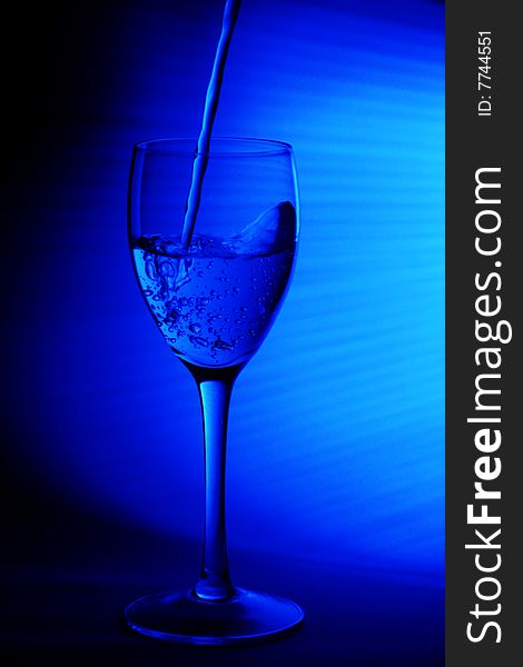 A glass of water being poured intoa wine glass with a blue background. A glass of water being poured intoa wine glass with a blue background.