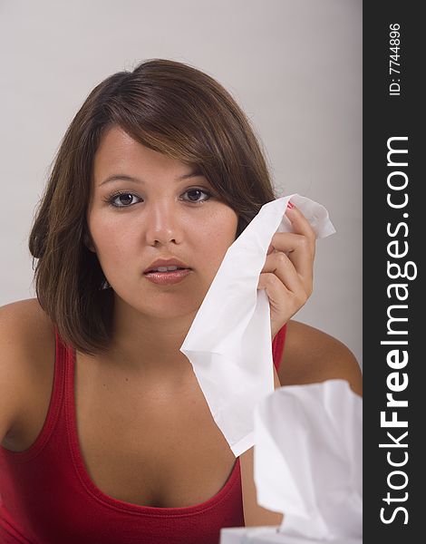 A young Asian girl with a cold blows her nose into a tissue. A young Asian girl with a cold blows her nose into a tissue