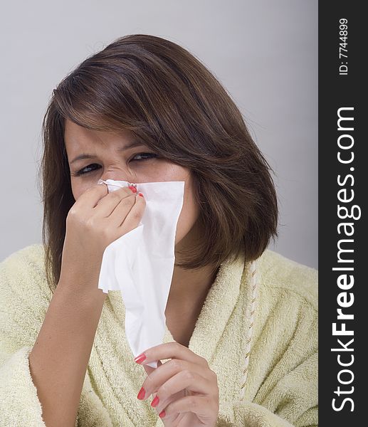 A young Asian girl with a cold blows her nose into a tissue. A young Asian girl with a cold blows her nose into a tissue