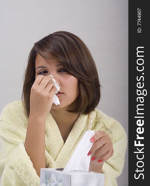 A young Asian girl with a cold blows her nose into a tissue. A young Asian girl with a cold blows her nose into a tissue