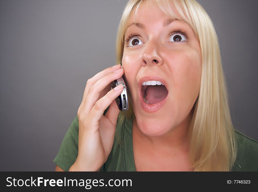 Stunned Blond Woman Using Cell Phone Against a Grey Background.