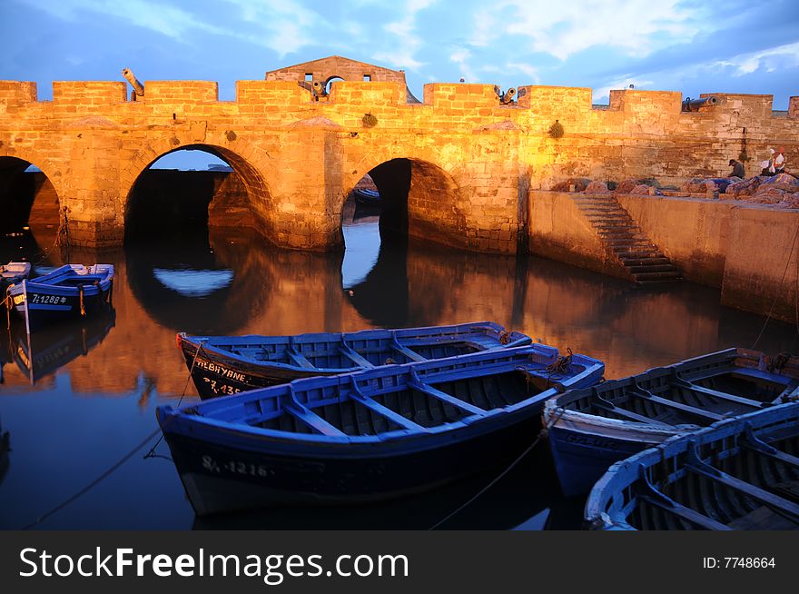Blue fishing boats in a harbour photographed against the ramparts of Essaquirra, Morocco
