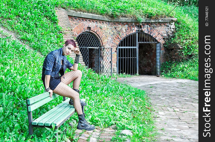 Punk girl sitting on the bench near old abandoned castle