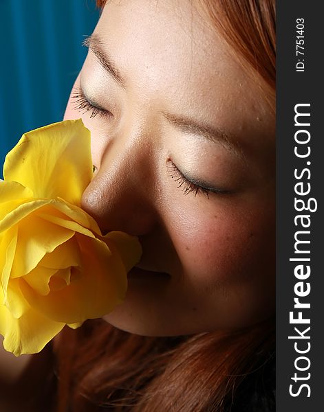 A photograph of a japanese girl smelling a yellow rose.