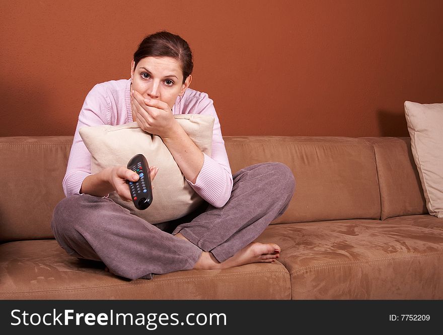 A young woman sits in front of a TV with the remote control in her hand on a couch. A lot of copyspace left. She seems to be afraid. A young woman sits in front of a TV with the remote control in her hand on a couch. A lot of copyspace left. She seems to be afraid.