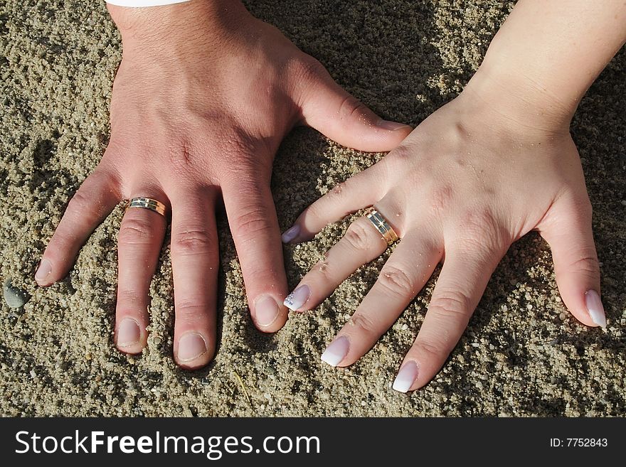 Sign on the sand, two hands and wedding rings