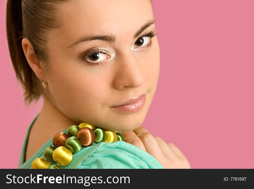 The beautiful young woman with a beads on a pink background