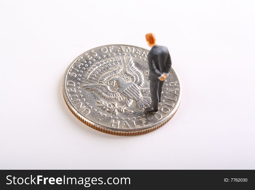 Miniature businessman looking down at the tails side of a half dollar.