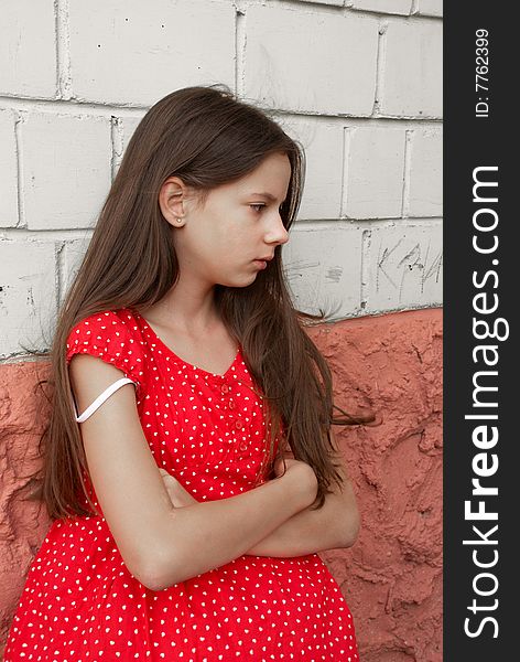 Beautiful sad girl in red dress  in front of brick wall. Beautiful sad girl in red dress  in front of brick wall