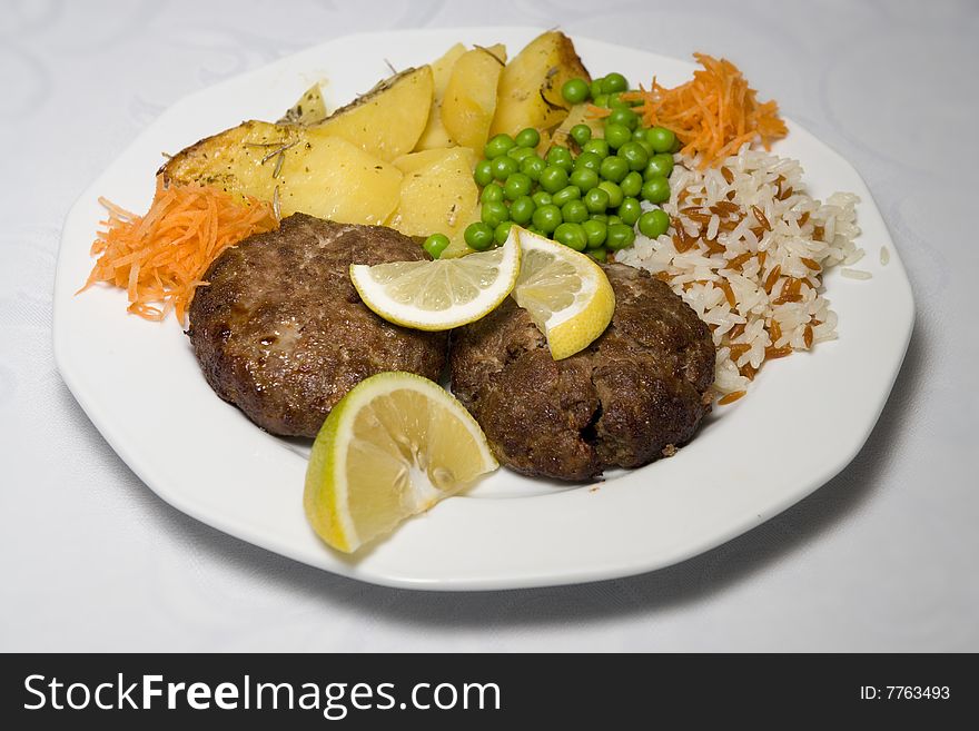 Two beefsteaks on the plate with potato's rice carrots pea and lemon. Two beefsteaks on the plate with potato's rice carrots pea and lemon