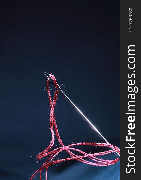 Close-up of steel needle with red thread on dark background. Close-up of steel needle with red thread on dark background