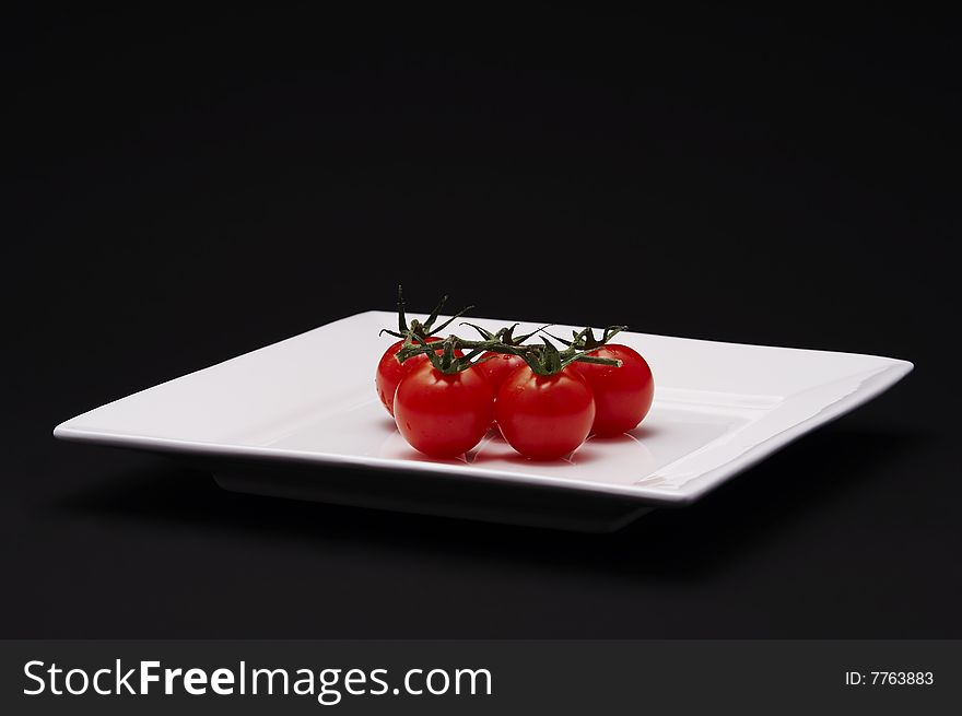 Five cherry tomatoes on a white plate with black background.