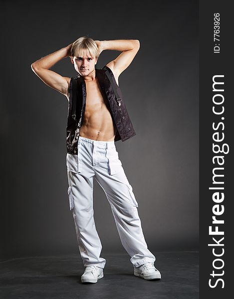 Young dancer in white trousers posing over dark background