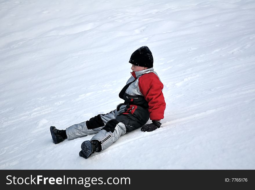 A boy slipped and sits on the snow