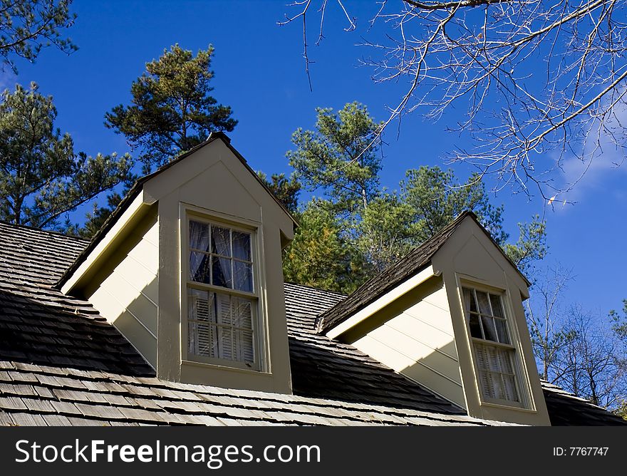 Two dormers on a wood shingle roof against blue sky. Two dormers on a wood shingle roof against blue sky