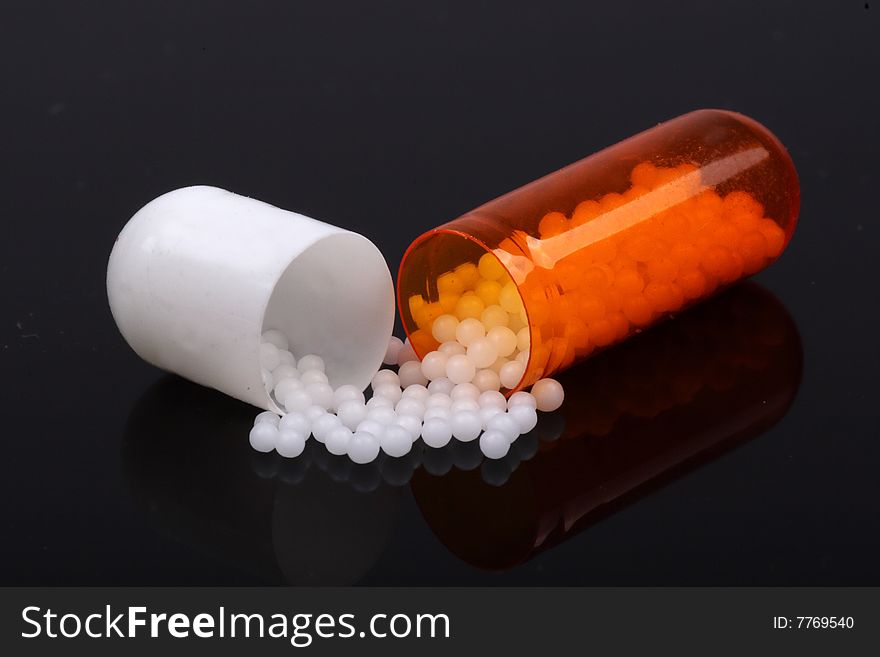 Close-up of a capsules of medication. It has been opened and the contents have spilled out. Black background.