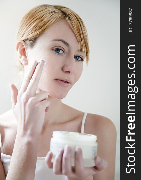 Young woman applying cream on her face. Young woman applying cream on her face.