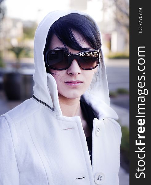 Attractive young woman on a cold winters day wearing designer white coat and stylish big sunglasses. Attractive young woman on a cold winters day wearing designer white coat and stylish big sunglasses