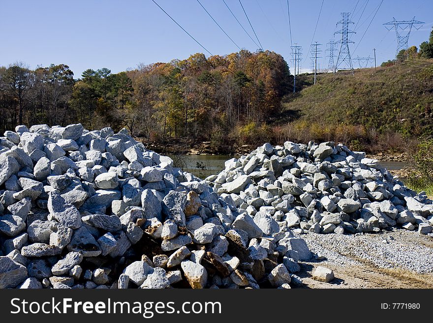 Two piles of granite blocks by a river near electric power lines. Two piles of granite blocks by a river near electric power lines