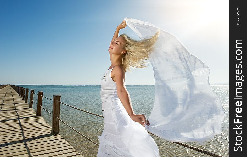 Blond woman with white shawl relaxing near the sea