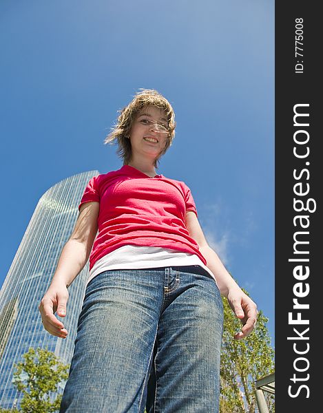 Portrait of a teen girl in casual clothing taken from a low angle with a modern building, trees and a blue sky in the background. Portrait of a teen girl in casual clothing taken from a low angle with a modern building, trees and a blue sky in the background