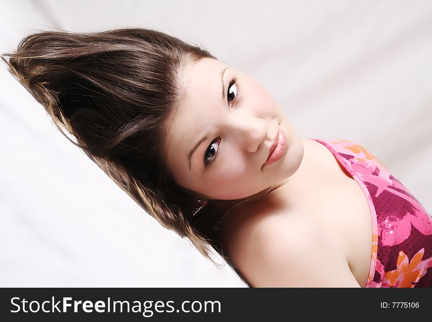 Teen girl laying on her back on white soft background wearing a colorful dress looking straight into the camera and smiling. Teen girl laying on her back on white soft background wearing a colorful dress looking straight into the camera and smiling