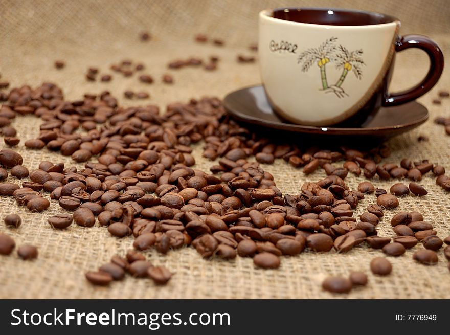 Coffee beans on focus and cup with cofee at the background. Coffee beans on focus and cup with cofee at the background