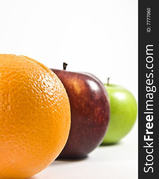 An orange, red apple and green apple lined up showing half of their shapes; the focus is on the orange while the rest are slightly blurred. An orange, red apple and green apple lined up showing half of their shapes; the focus is on the orange while the rest are slightly blurred