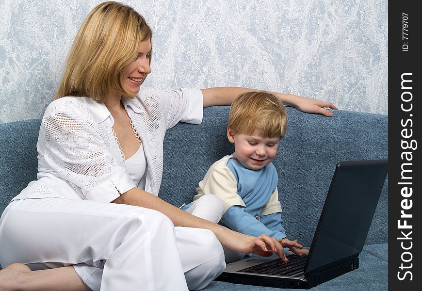 Young mum with the small beautiful boy together sit near laptop. Young mum with the small beautiful boy together sit near laptop