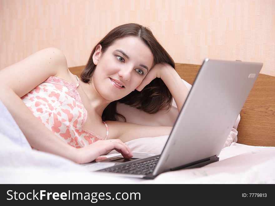 Smiling girl lays in bed with laptop