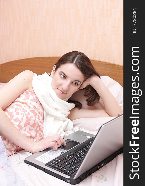 Girl with a sick throat lays in bed with laptop