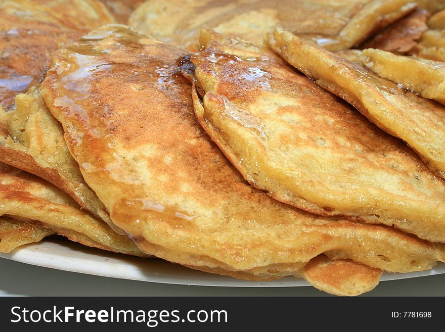 A closeup of a stack pancakes on a platter drizzled with syrup.