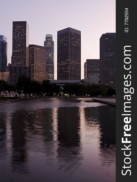 Los Angeles skyline at dusk with buildings reflected in water pool.