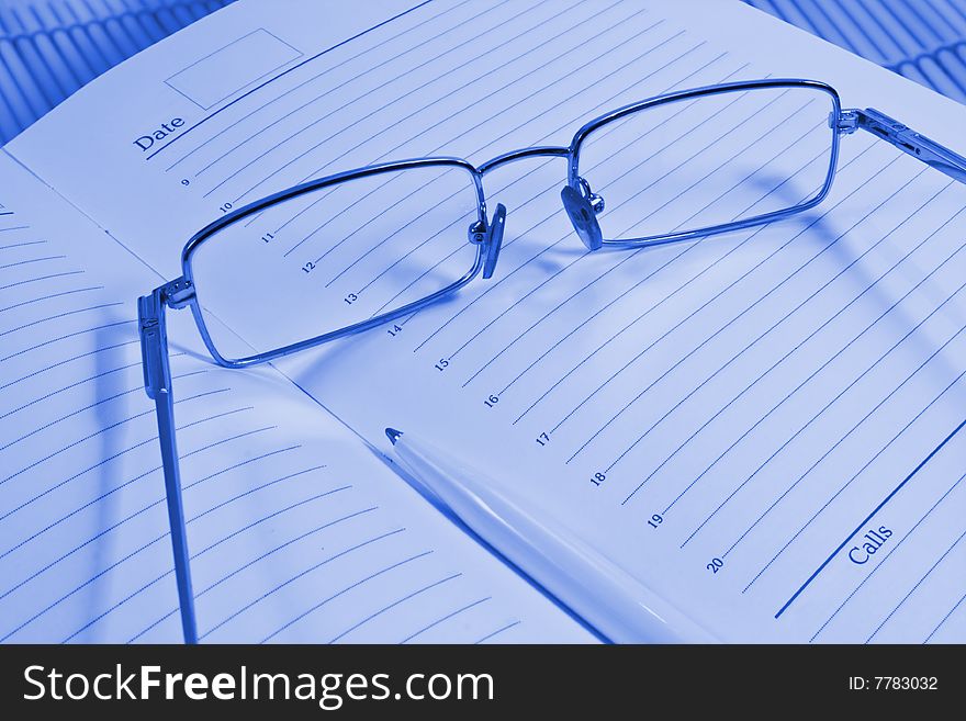 Glasses, pen and notebook, photographed close up.