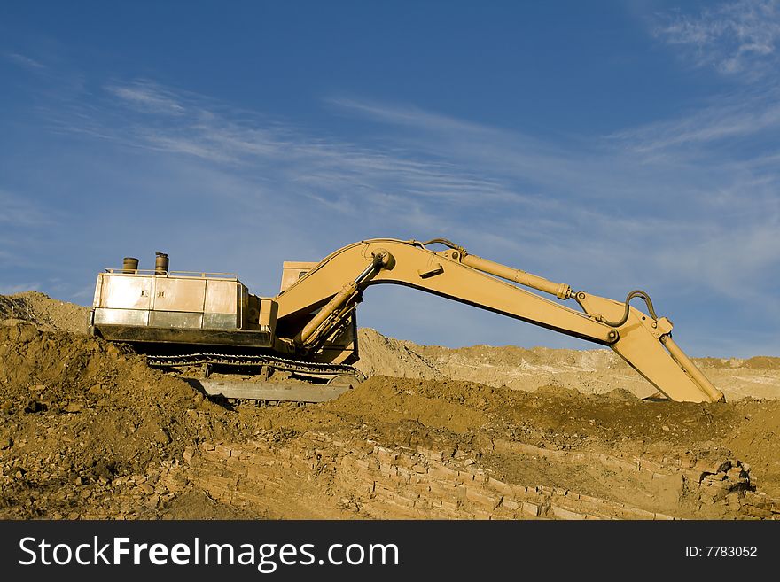 Excavator on construction site with dirt against blue sky.