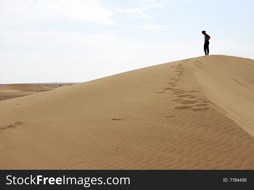 A woman walks along the ridge of a sand dune in the vast Peruvian desert. A woman walks along the ridge of a sand dune in the vast Peruvian desert