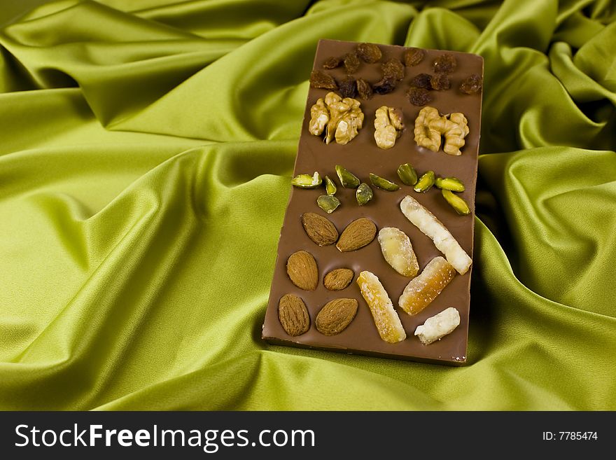 A chocolate - nougat bar with walnuts, almonds, raisins, pistachios and candied orange on green satin background. A chocolate - nougat bar with walnuts, almonds, raisins, pistachios and candied orange on green satin background.