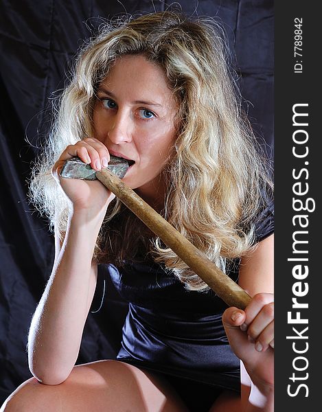 Young woman bites a hammer against a black background. Young woman bites a hammer against a black background