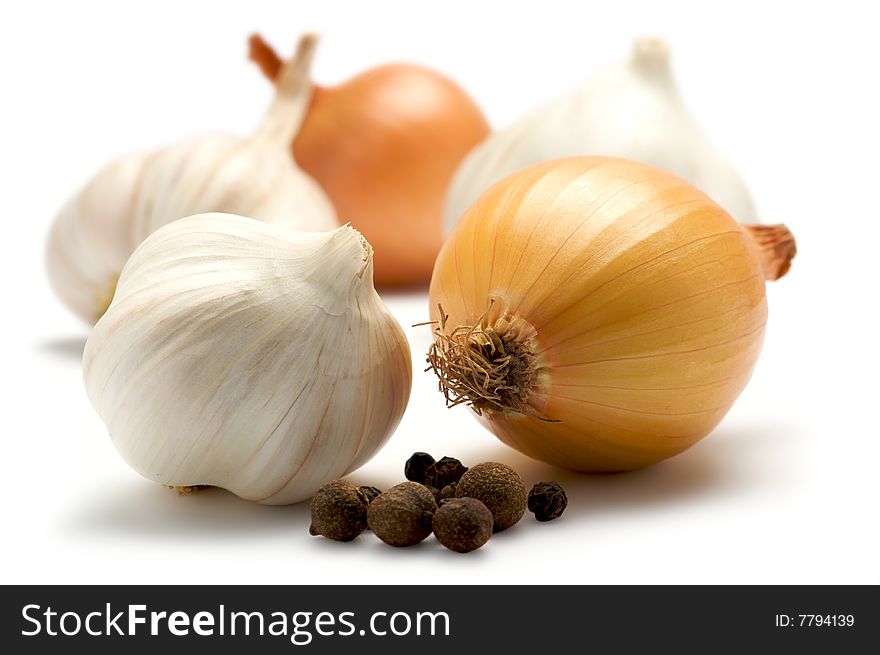 A few onions and garlic are isolated on a white background. Background blurred. In the foreground is the black pepper. A few onions and garlic are isolated on a white background. Background blurred. In the foreground is the black pepper.