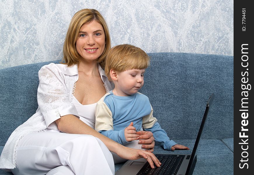 Young mum with the small beautiful boy together sit near laptop. Young mum with the small beautiful boy together sit near laptop