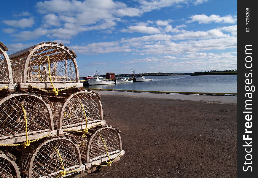 Lobster traps stacked on the wharf with fishing boats and harbor in the background and space for copy. Lobster traps stacked on the wharf with fishing boats and harbor in the background and space for copy.