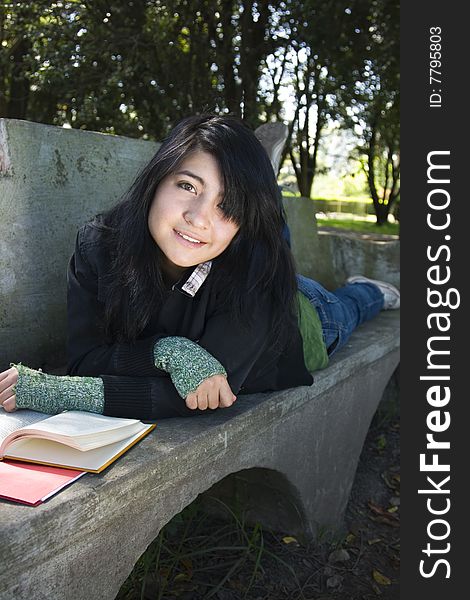 A teenager student smiles at the camera from a park bench. A teenager student smiles at the camera from a park bench.