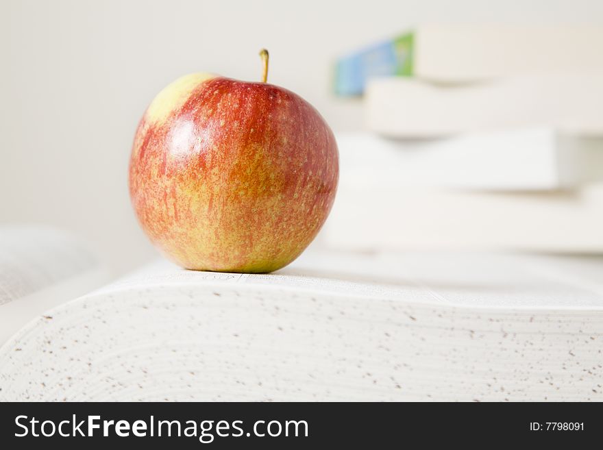 Open book with a red apple. Stack of books in the background. Open book with a red apple. Stack of books in the background